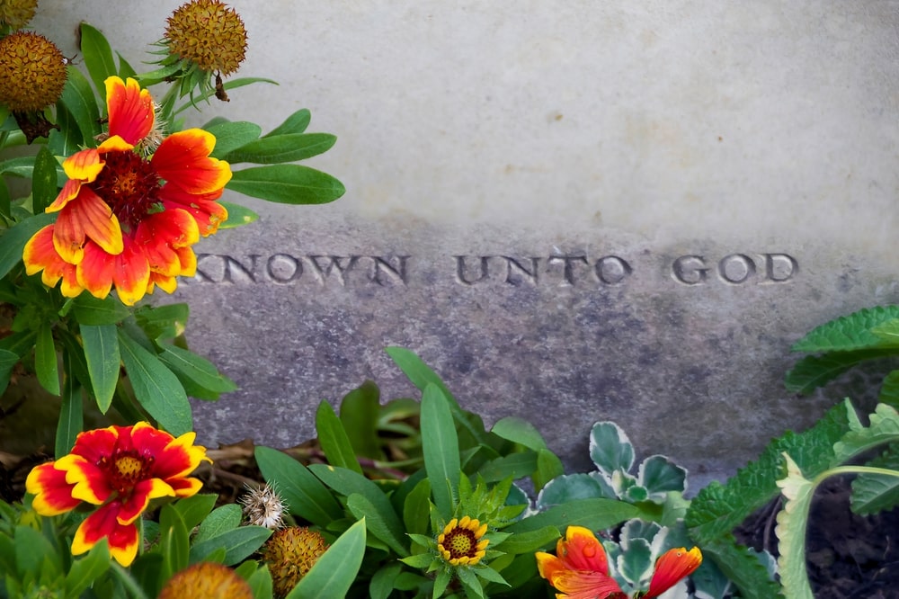 Plack that says "Known Unto God" surrounded by orange and yellow flowers