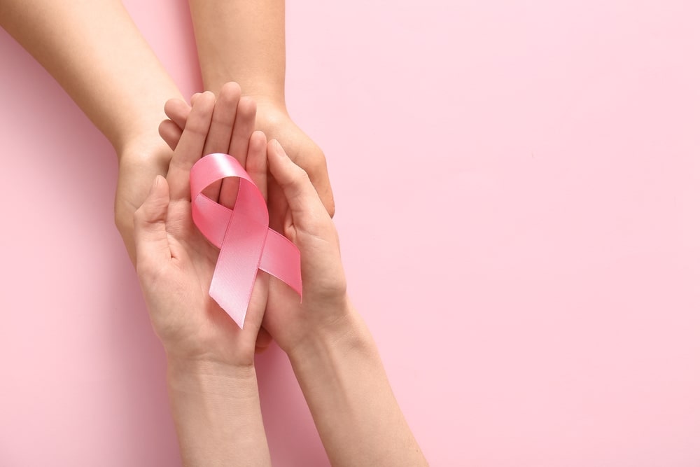 Two women holding a pink breast cancer awareness ribbon against a pink background