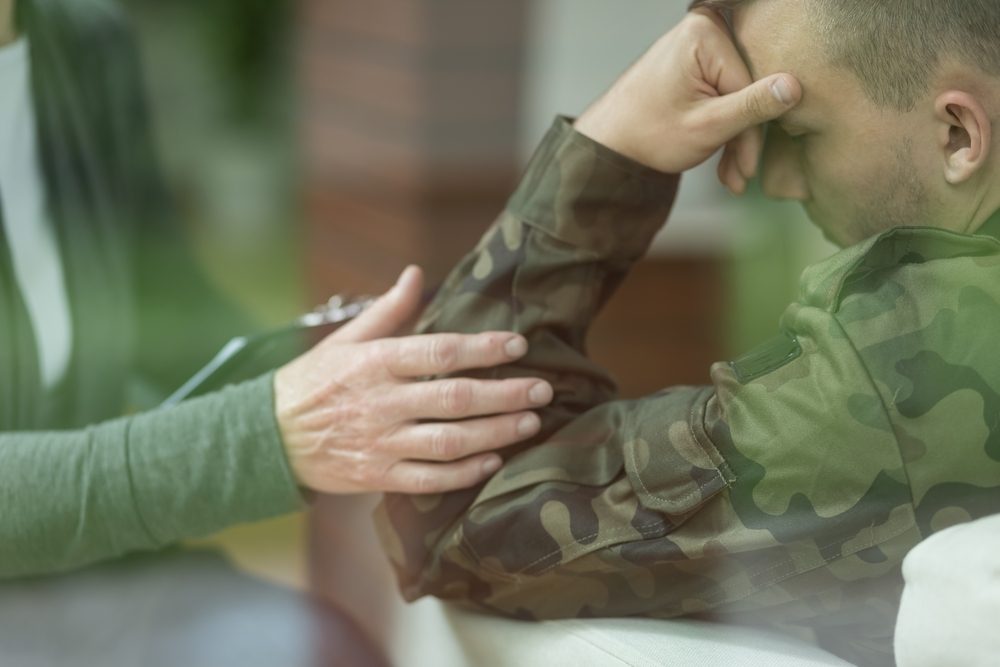 Woman comforting male solider, who looks distraught and has a hand to his face