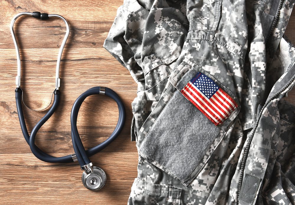 American military uniform with American flag patch lying on wooden surface. Stethoscope lying beside it.