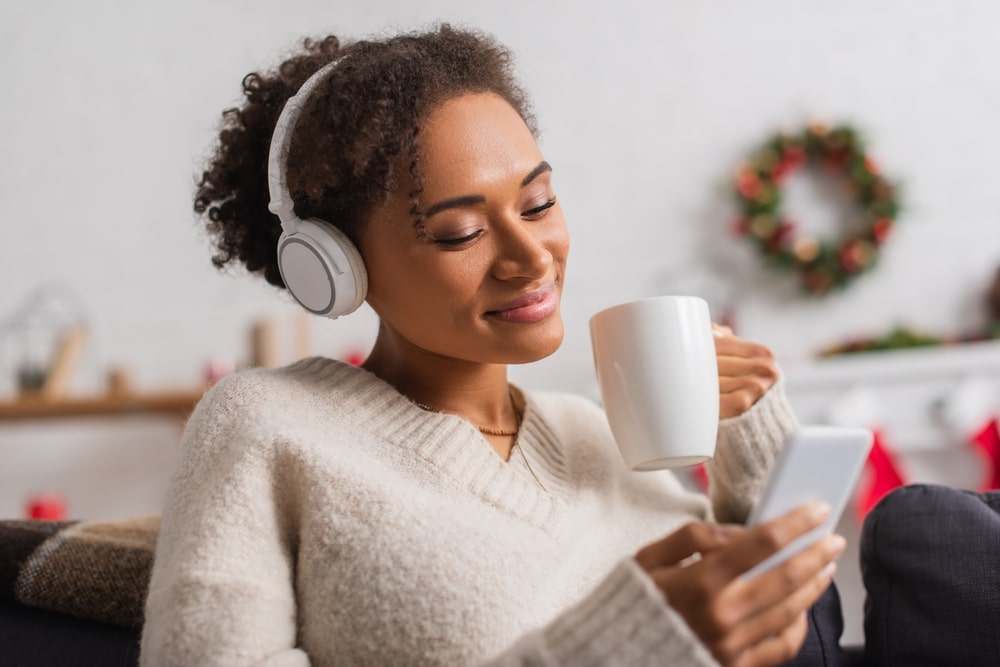 Young woman sitting on couch at home at Christmas, listening to music on headphones