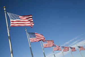 Six American flags waving in the breeze against a blue sky