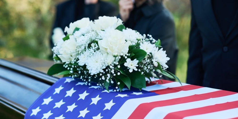 Spray of white flowers resting on a casket covered in an American flag