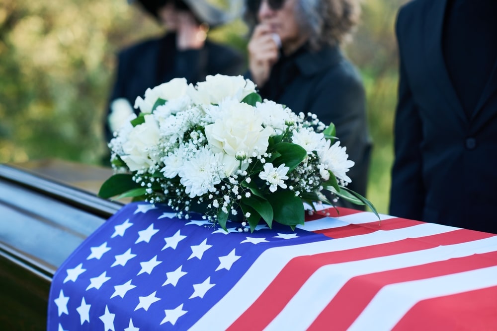 Spray of white flowers resting on a casket covered in an American flag
