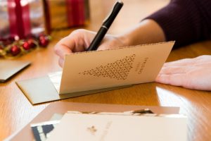 Woman sitting at table, writing a message in a Christmas card