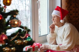 Person sitting at window, next to Christmas tree, looking quiet and sad