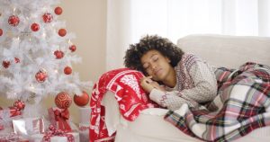 Young woman taking a nap on the couch with Christmas tree nearby, participating in self-care