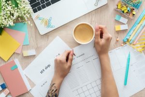 Person sitting at table with calendars and cup of coffee in front