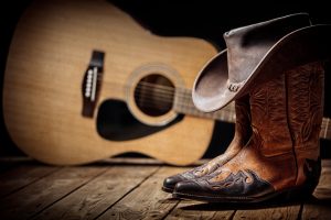 Cowboy boots with hat in foreground with guitar in background
