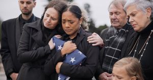 Gathering of mourners supporting grieving woman, who is holding a burial flag