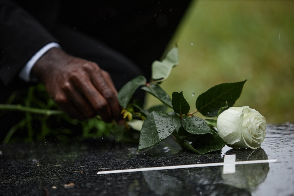 Man placing white rose reverently on top of casket