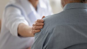 Professional resting caring hand on shoulder of grieving person