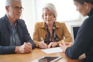 Mature couple sitting down with funeral professional, signing papers