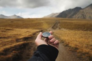 Focus on hand holding a compass pointed at a high road outdoors