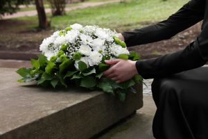 Person wearing black placing a spray of white flowers at a loved one's grave