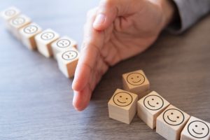 Tiles with happy and sad faces printed on them resting on a table with a person's hand splitting them apart