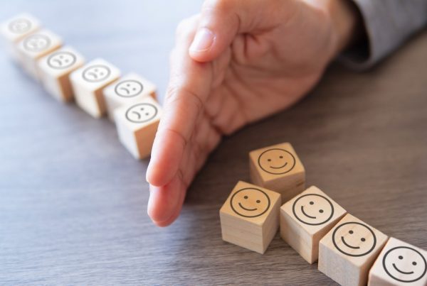 Tiles with happy and sad faces printed on them resting on a table with a person's hand splitting them apart