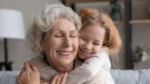 Grandmother and granddaughter sitting on couch and hugging with smiles on their faces