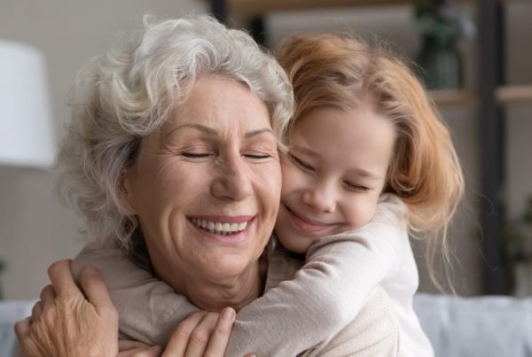 Grandmother and granddaughter sitting on couch and hugging with smiles on their faces