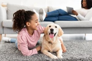 Young girl in pink shirt lying on floor with golden retriever dog