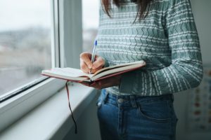 Woman in striped sweater writing a list in a journal