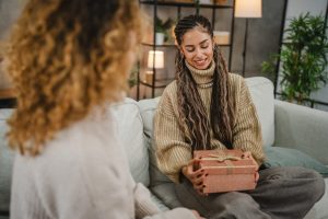 Woman gives gift to grieving friend while they both sit on a couch