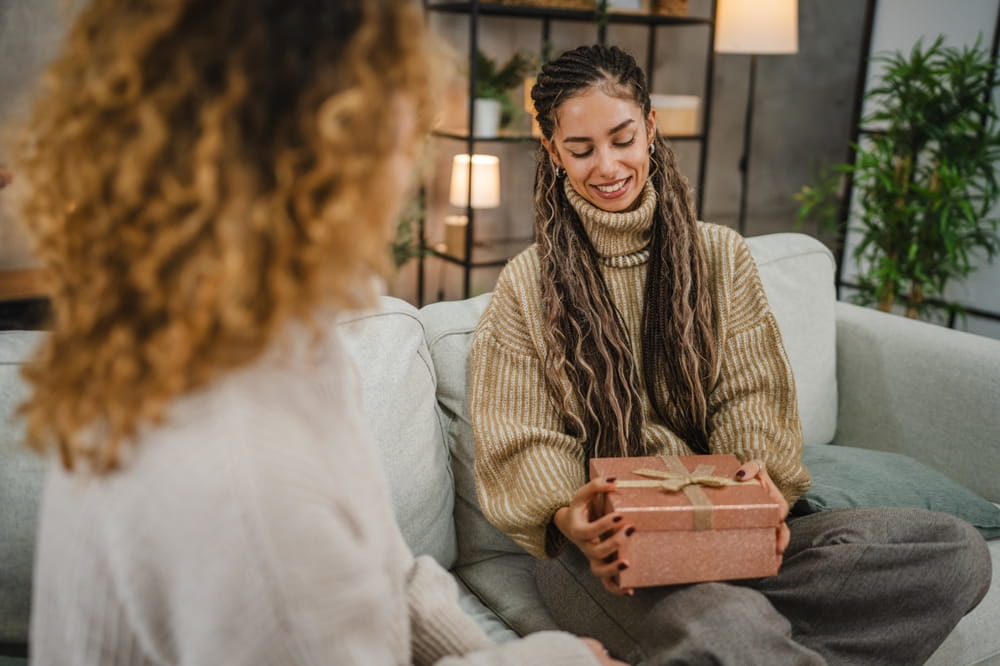 Woman gives gift to grieving friend while they both sit on a couch