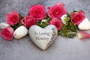 Heart stone that says "In Loving Memory" surrounded by bright pink flowers