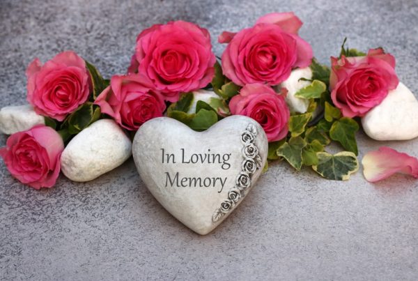 Heart stone that says "In Loving Memory" surrounded by bright pink flowers