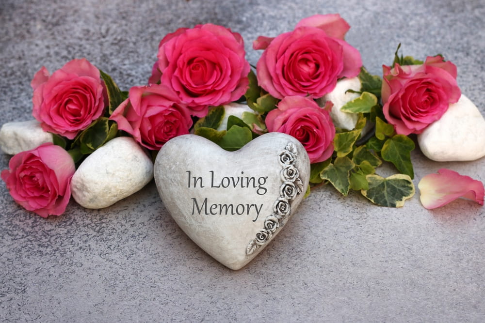 Heart stone that says "In Loving Memory" surrounded by bright pink flowers