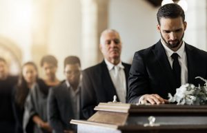 Man standing at front of receiving line as he rests a hand on a closed casket and pays his respects