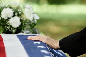 Woman resting hand on a flag-draped casket with white flowers in background