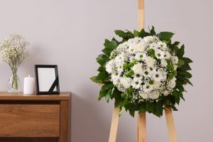 Standing funeral spray of white flowers with memorial candle and photo on a table behind