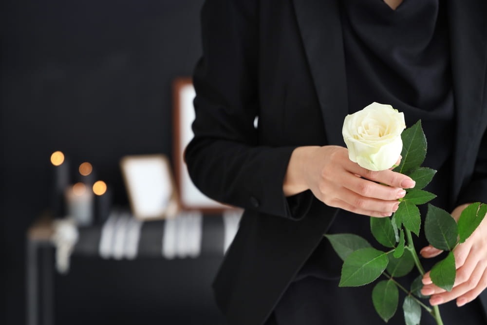 Woman in black holding white rose in her hands with memorial table behind her