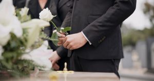 Man standing next to casket with white rose in his hands