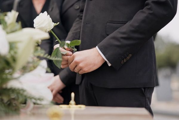 Man standing next to casket with white rose in his hands