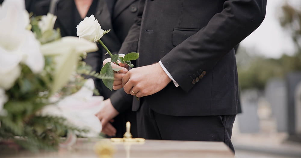 Man standing next to casket with white rose in his hands