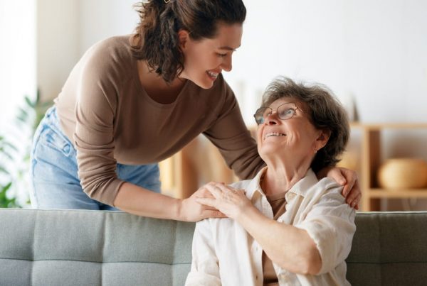 Senior woman sitting on couch and smiling up at adult daughter