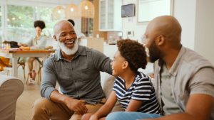 Smiling senior man sitting with adult son and teenage grandson with the kitchen behind them