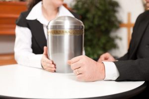 Man and woman talking with a metal cremation urn resting on the table between them
