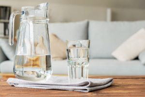 Pitcher of water and glass sitting on a coffee table in front of a couch