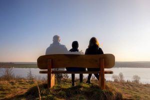 Family of three sitting on a bench outside, but the father is slightly transparent indicating that he is not actually present