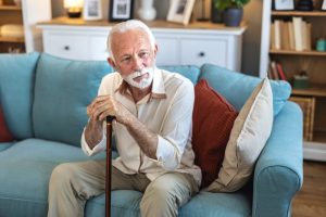 Man sitting on couch holding a cane to help with preventing falls