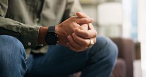 Man in green shirt and jeans sitting alone with clasped hands