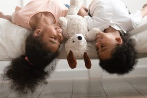 Two children laying on bed with a stuffed animal between them
