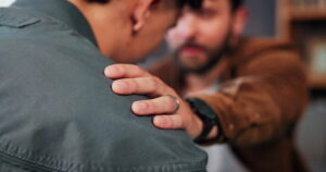 Man in brown shirt resting a comforting hand on his grieving friend's shoulder