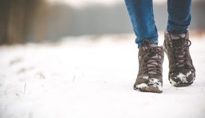 Focus on jeans and brown winter boots of a person walking on snowy path