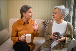 Two women sitting on a couch at home, talking and drinking from mugs
