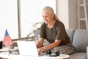 Mature female service member sitting on couch at home, working on her laptop
