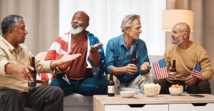 group of four men who may be veterans sitting on couch, talking as they hold American flags